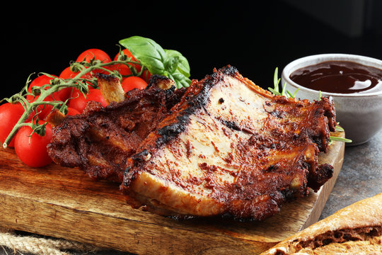 Spicy hot grilled spare ribs from a summer BBQ served with fresh tomatoes on an old vintage wooden cutting board