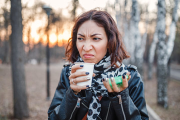 Shocked woman tries disgusting coffee or tea from a disposable takeaway coffee outdoors