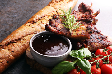 Spicy hot grilled spare ribs from a summer BBQ served with fresh tomatoes on an old vintage wooden cutting board