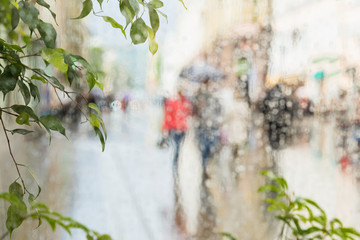 Raindrops on window glass, few unrecognizable people rush home under umbrellas, abstract blurred...