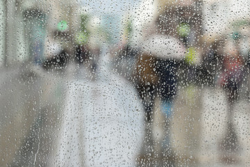 Abstract background of two young people under umbrella, walk on road in city in rain. Water drops on glass. Intentional motion blur. Concept of seasons, modern city.