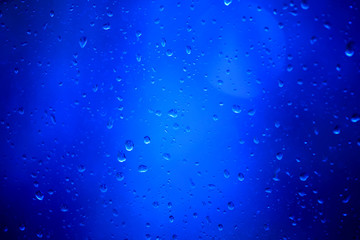 Naklejka na ściany i meble Drops of rain on a glass on a blue background