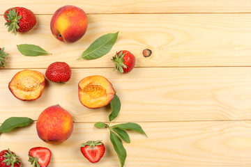peach fruit with strawberry and green leaf on light wooden background. top view with copy space