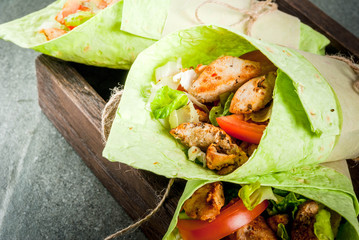 Mexican food. Healthy eating. Wrap sandwich: green lavash tortillas with spinach, fried chicken, fresh greens salad, tomatoes, yoghurt sauce. Wooden tray, dark stone table. Copy space
