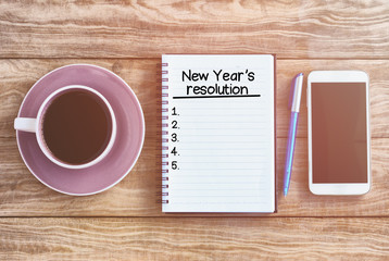 New year's resolution list on note pad, wood table with coffee, pen and smart phone retro styled.