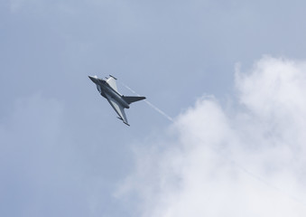 Modern jet fighter flying high against the gray sky with some clouds.