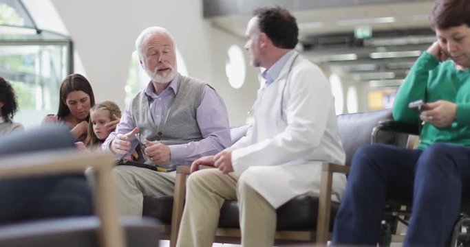 Senior Male talking to Doctor in a crowded hospital waiting room 