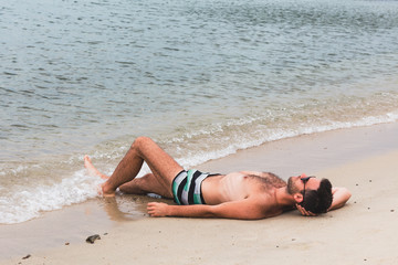 Young man lying on the beach by the water
