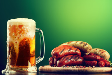 Mug of beer with grilled sausages on green background. Oktoberfest drink and food