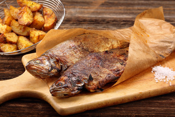 grilled fish with potatoes wrapped in paper on wooden background