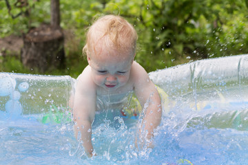 Happy infant kid playing in the the swimming pool in the garden. Water splash. Summer vacation concept