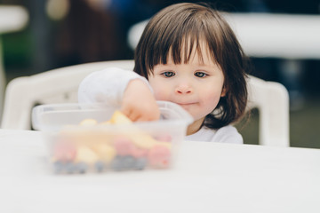 adorable little girl eating healthy snack from food container. strawberry, blueberry, apple