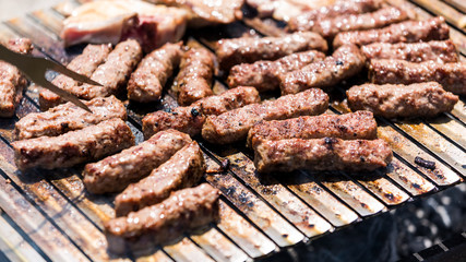 Grilling minced meat on a barbecue grill with coal; outdoors picnic with minced pork meat rolls (also known as mici,   mititei, cevapi or cevapcici)