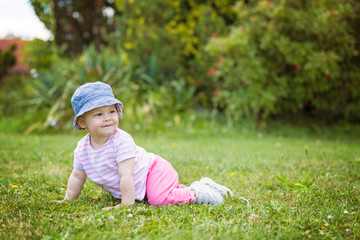 Fourteen months old baby girl crawling on the grass on the sunny summer day