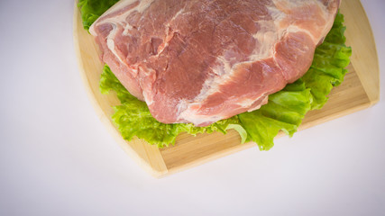 Raw cervical carbonate of pork on cutting board with leaves of green salad, isolated on white background