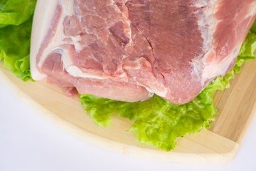 Raw cervical carbonate of pork on cutting board with leaves of green salad, isolated on white background