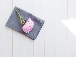 Pink peony on folded grey linen napkin on white wooden background