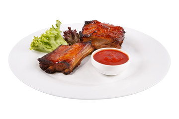 Meat ribs on a white plate with sauce and lettuce leaves