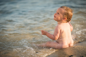 Happy adorable little girl sitting in water on sand beach
