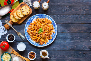 Fusilli pasta with tomato sauce, tomatoes, onion, garlic, dried paprika, olives, pepper and olive oil, on a wooden background.