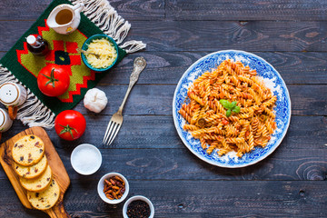 Fusilli pasta with tomato sauce, tomatoes, onion, garlic, dried paprika, olives, pepper and olive oil, on a wooden background.