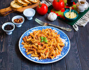 Fusilli pasta with tomato sauce, tomatoes, onion, garlic, dried paprika, olives, pepper and olive oil, on a wooden background.