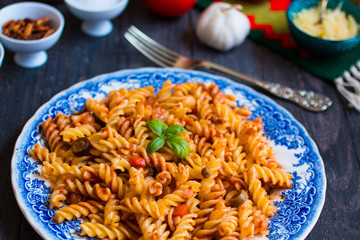 Fusilli pasta with tomato sauce, tomatoes, onion, garlic, dried paprika, olives, pepper and olive oil, on a wooden background.