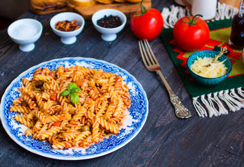 Fusilli pasta with tomato sauce, tomatoes, onion, garlic, dried paprika, olives, pepper and olive oil, on a wooden background.