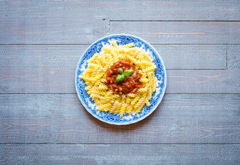 Fusilli pasta with tomato sauce, tomatoes, onion, garlic, dried paprika, olives, pepper and olive oil, on a wooden background.