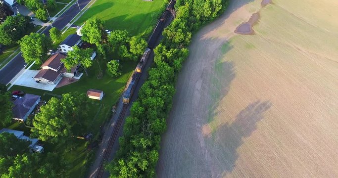 Coal train rolls between small town and farm field, aerial view.
