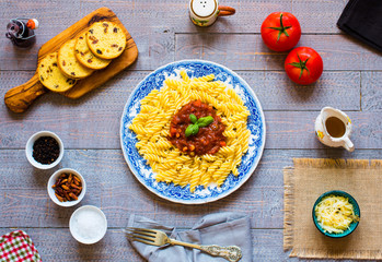 Fusilli pasta with tomato sauce, tomatoes, onion, garlic, dried paprika, olives, pepper and olive oil, on a wooden background.