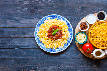 Fusilli pasta with tomato sauce, tomatoes, onion, garlic, dried paprika, olives, pepper and olive oil, on a wooden background.