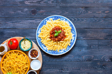Fusilli pasta with tomato sauce, tomatoes, onion, garlic, dried paprika, olives, pepper and olive oil, on a wooden background.