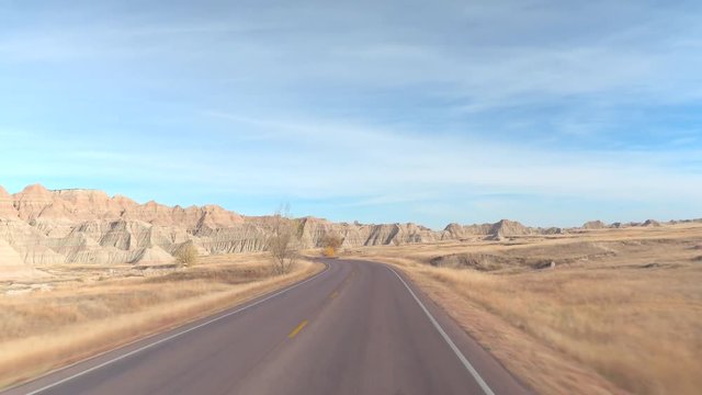 FPV: Driving along the empty road winding towards amazing Badlands landscape with rocky sandstone mountains. Traveling across Badlands grassland desert in South Dakota. Road trip across United States