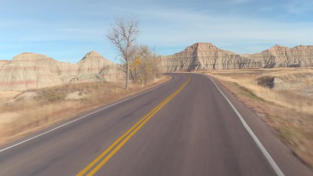 FPV: Driving along the empty road winding past amazing Badlands landscape with rocky sandstone mountains. Traveling across the Badlands grassland desert in South Dakota. Road trip across United States