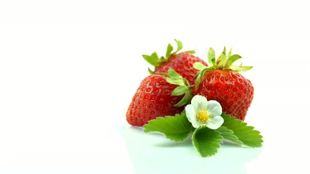 Strawberry closeup. Ripe berries with leaves and blooming flower. Rotation over white background. 4K UHD video 3840X2160