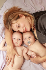 indoor portrait of young happy smiling mother with her twin babies at home