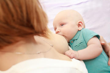 indoor portrait of mother breast feeding and hugging her baby at home