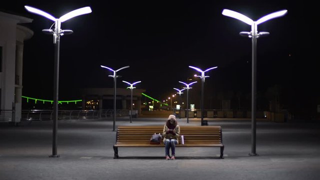Frozen lady waiting for last bus at empty night station, checking timetable