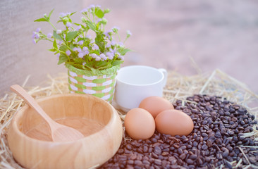 Fototapeta na wymiar Equipment of food and drink in the morning, such as eggs, coffee beans, And there are cups, wooden bowl, white glass and flowers as part of the scene. Food concept and Copy space.