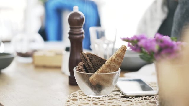 Close up of a hand of a young unrecognizable woman taking a piece of bread from a glass bowl in a cafe while chatting with her friend and waiting for her order. Locked down real time close up shot