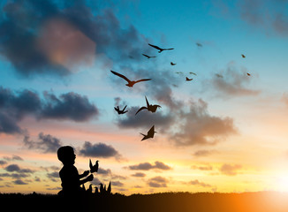 Fototapeta na wymiar Silhouette Children playing paper birds that fly with real birds freely over blurred natural. Imagination is more important to the development of children's brains. Learning and freedom concept.
