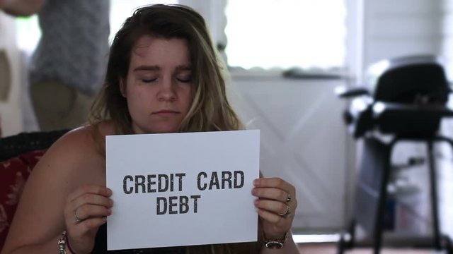 Frustrated woman holds up credit card debt sign while husband yells in background