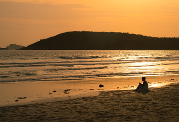 Naklejka na ściany i meble Women sitting on the beach in Chonburi province of Thailand at sunset.