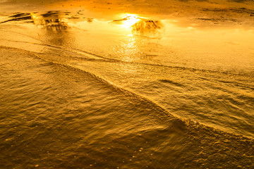 Golden light reflecting off a water wave at the sea and sand on sunset. Pure Gold Tone