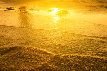 Golden light reflecting off a water wave at the sea and sand on sunset. Pure Gold Tone