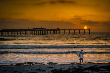 Obraz premium Surfer on California beach at sunset with pier