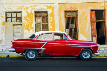 Vibrant red shiny car and ruined house in Cuba