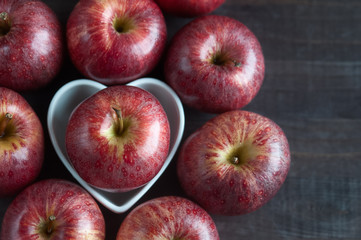 Red apples on the table, heart-shaped dish. Harvest, a lot of apples. Fruits, antioxidants, vitamins.  love fruits, love apples