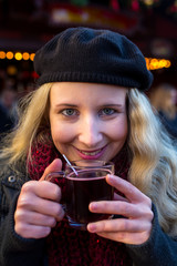 Junge Frau mit Wollmütze trinkt Glühwein auf dem Weihnachtsmarkt